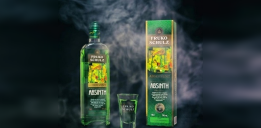 Láhev zeleného absintu Fruko-Schulz se skleničkou a dárkovým balením na tmavém pozadí s kouřovým efektem.
